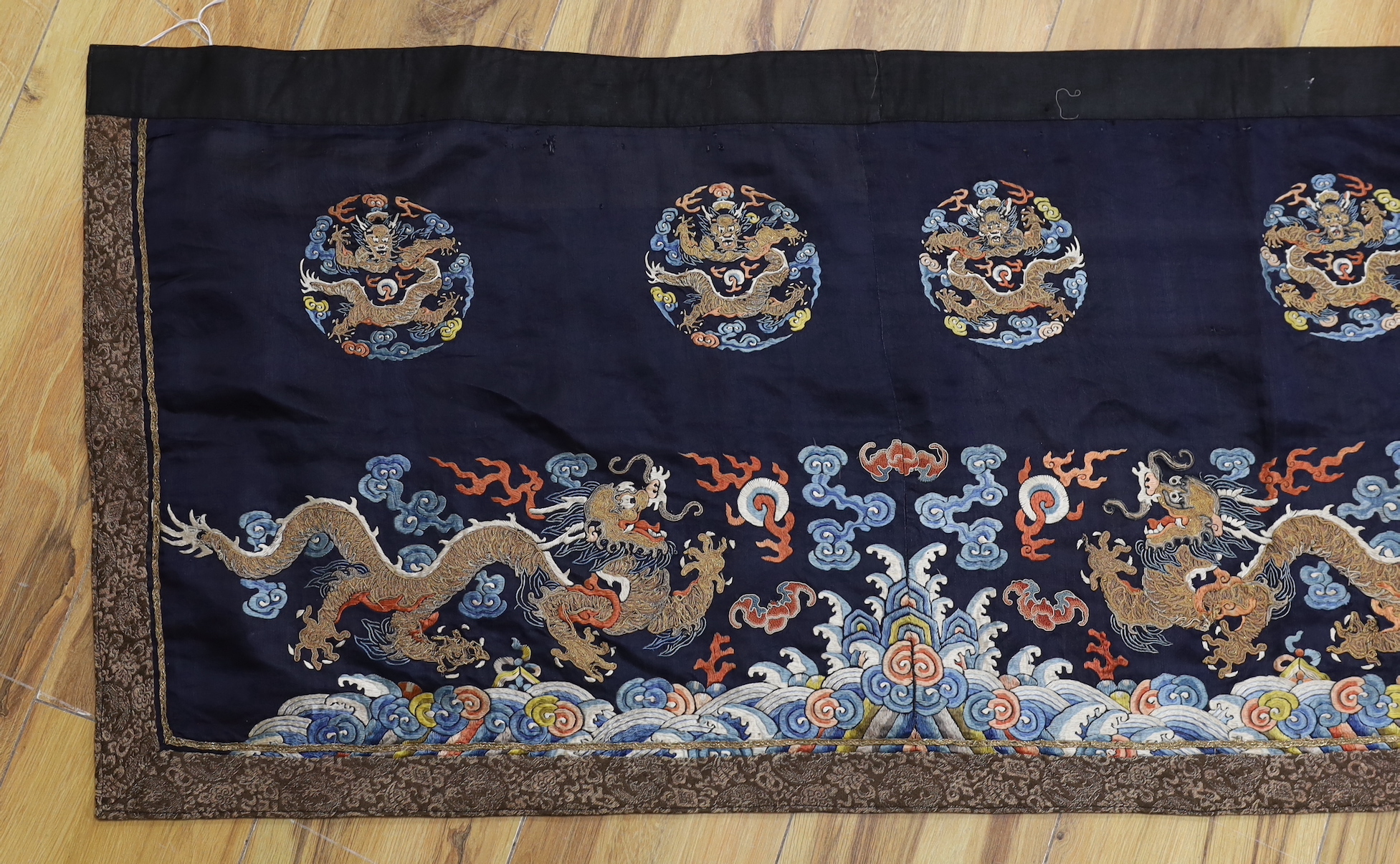A Chinese long dark blue ground ‘dragon’ altar cloth, late Qing dynasty, polychrome embroidered, celestial dragons and mons amongst stylised clouds, 300 x 50cm